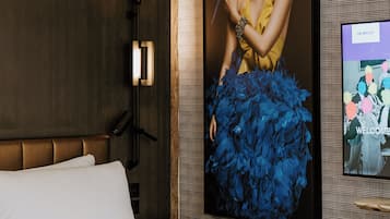 Una habitación de hotel moderna con una cama grande, un televisor montado en la pared y un retrato enmarcado de una mujer con un loro.