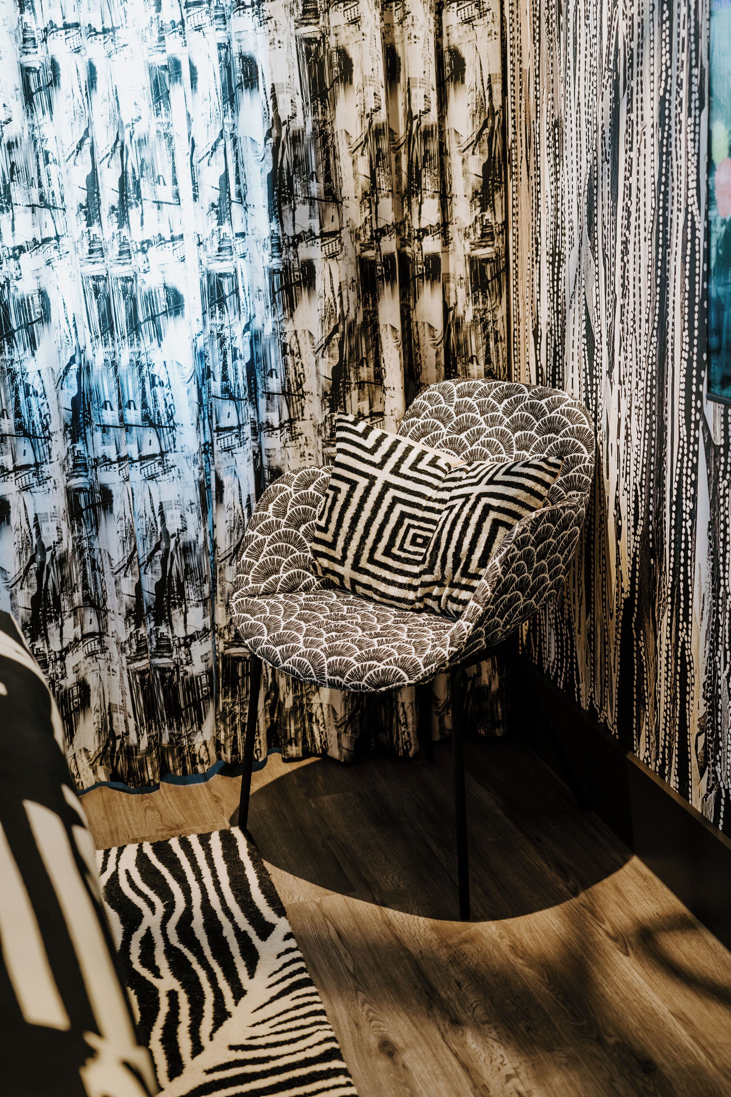 Une pièce moderne avec un plancher en bois aux lignes courbes, un fauteuil à motifs et un mur orné de rayures verticales.