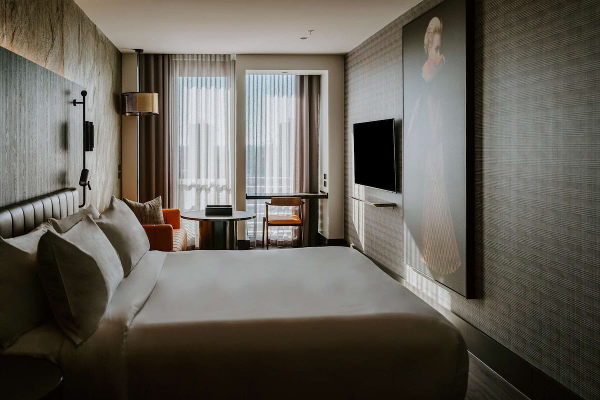 Une chambre d’hôtel avec un grand lit, un bureau, une chaise, une télévision et une fenêtre avec des rideaux.