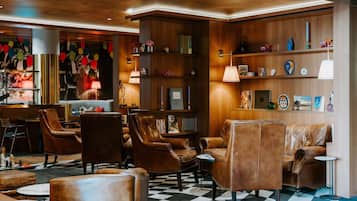 Een ontvangsthal met lederen fauteuils, een geruit vloerkleed, houten kasten met decoratieve objecten en een bar.