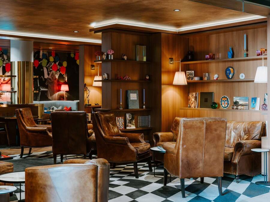 Een ontvangsthal met lederen fauteuils, een geruit vloerkleed, houten kasten met decoratieve objecten en een bar.