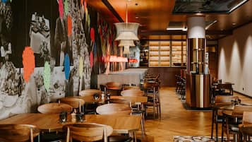 Un restaurante con mesas y sillas de madera, una zona de bar y una pared con decoraciones coloridas.