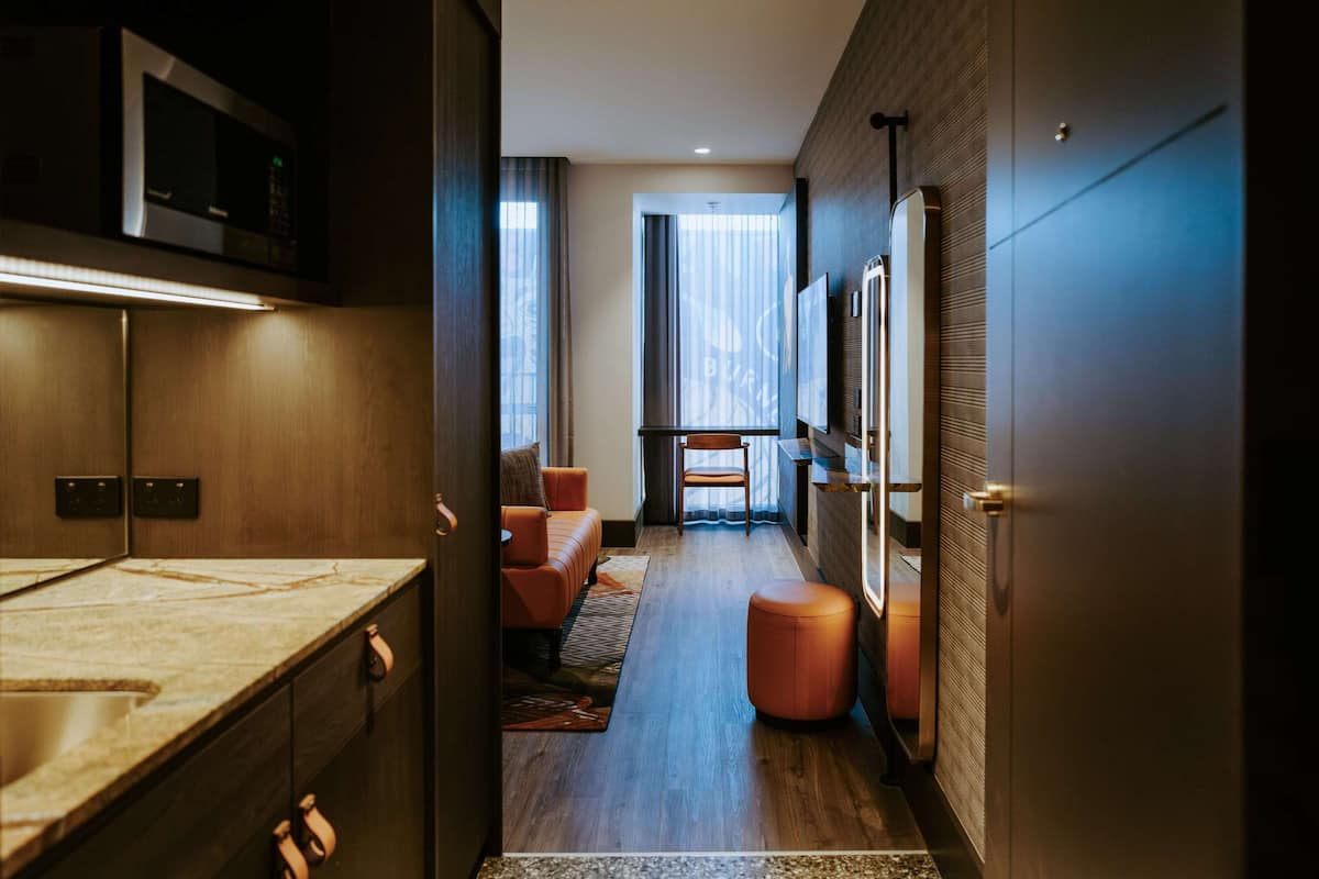 Un couloir d’hôtel moderne comprenant un coin cuisine, un espace salon et une grande fenêtre avec des rideaux.