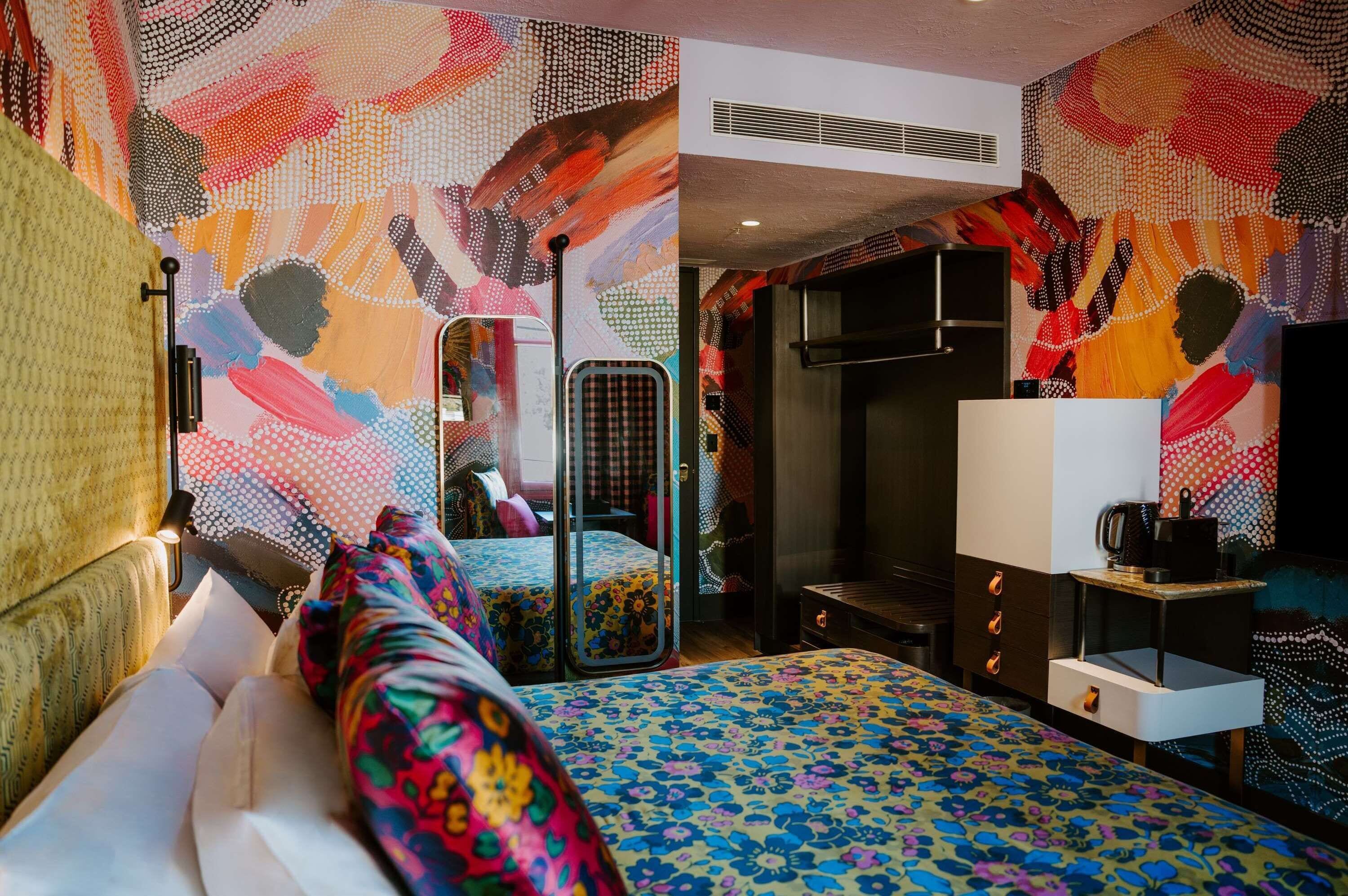 Une chambre d’hôtel avec un grand lit, un bureau, une chaise, une armoire et un miroir.