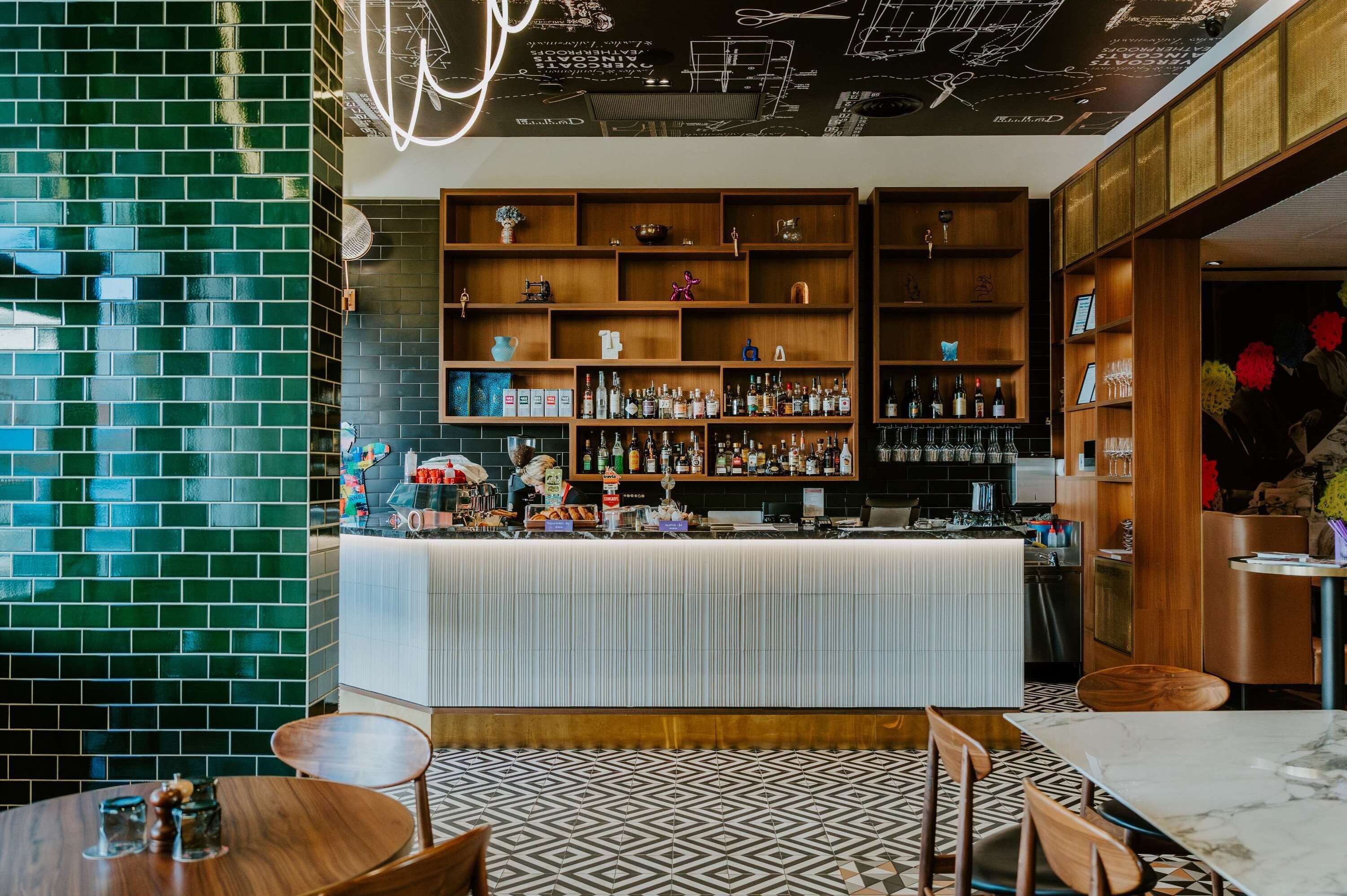 Una zona de bar con mostrador, estantes llenos de botellas y piso estampado.