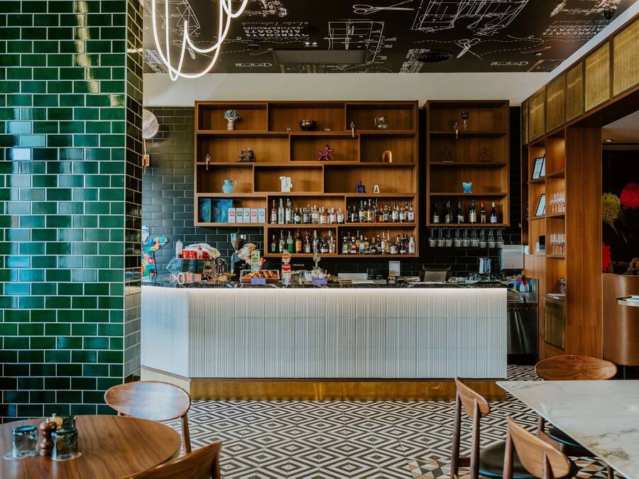 Una zona de bar con mostrador, estantes llenos de botellas y piso estampado.