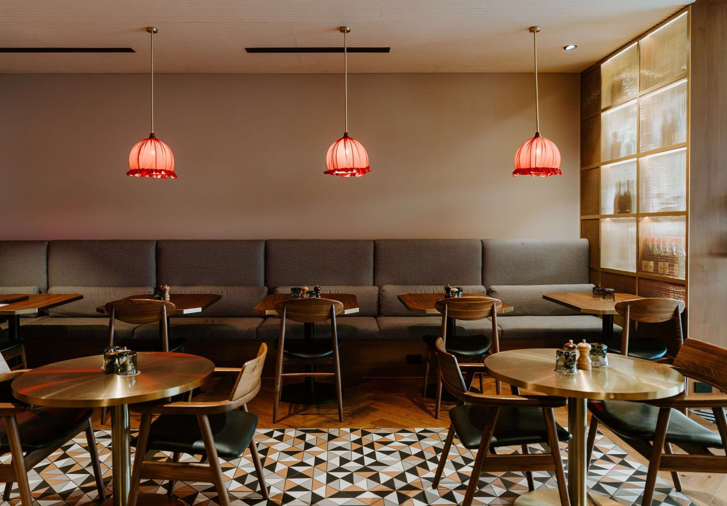 A restaurant interior with round tables, cushioned booths, and pendant lighting.