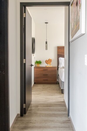 A hallway leading to a bedroom with a wooden dresser, a bed, and a hanging light fixture. - Apartment with exclusive access to the shopping center (Ciudad de México)