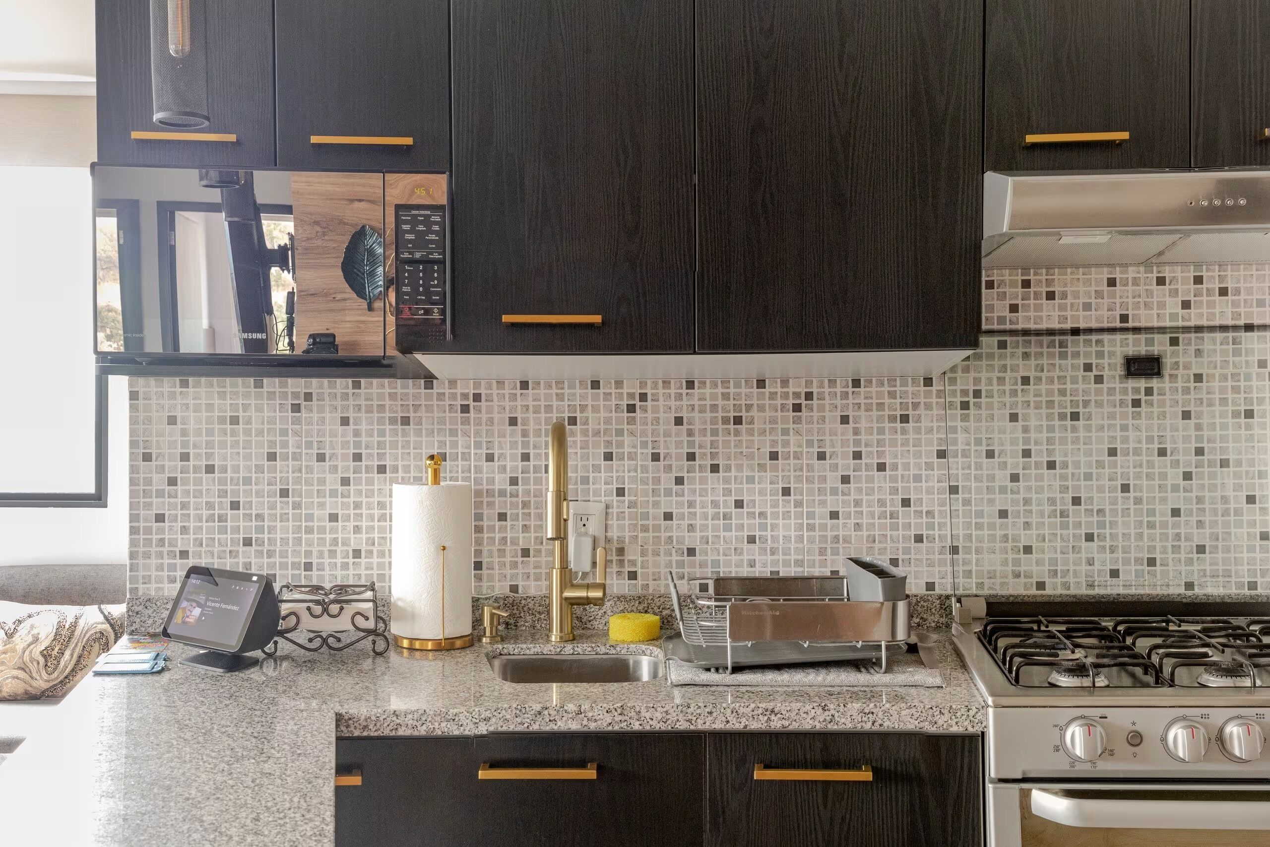 A modern kitchen with dark cabinetry, a microwave, a gas stove, and a tiled backsplash.