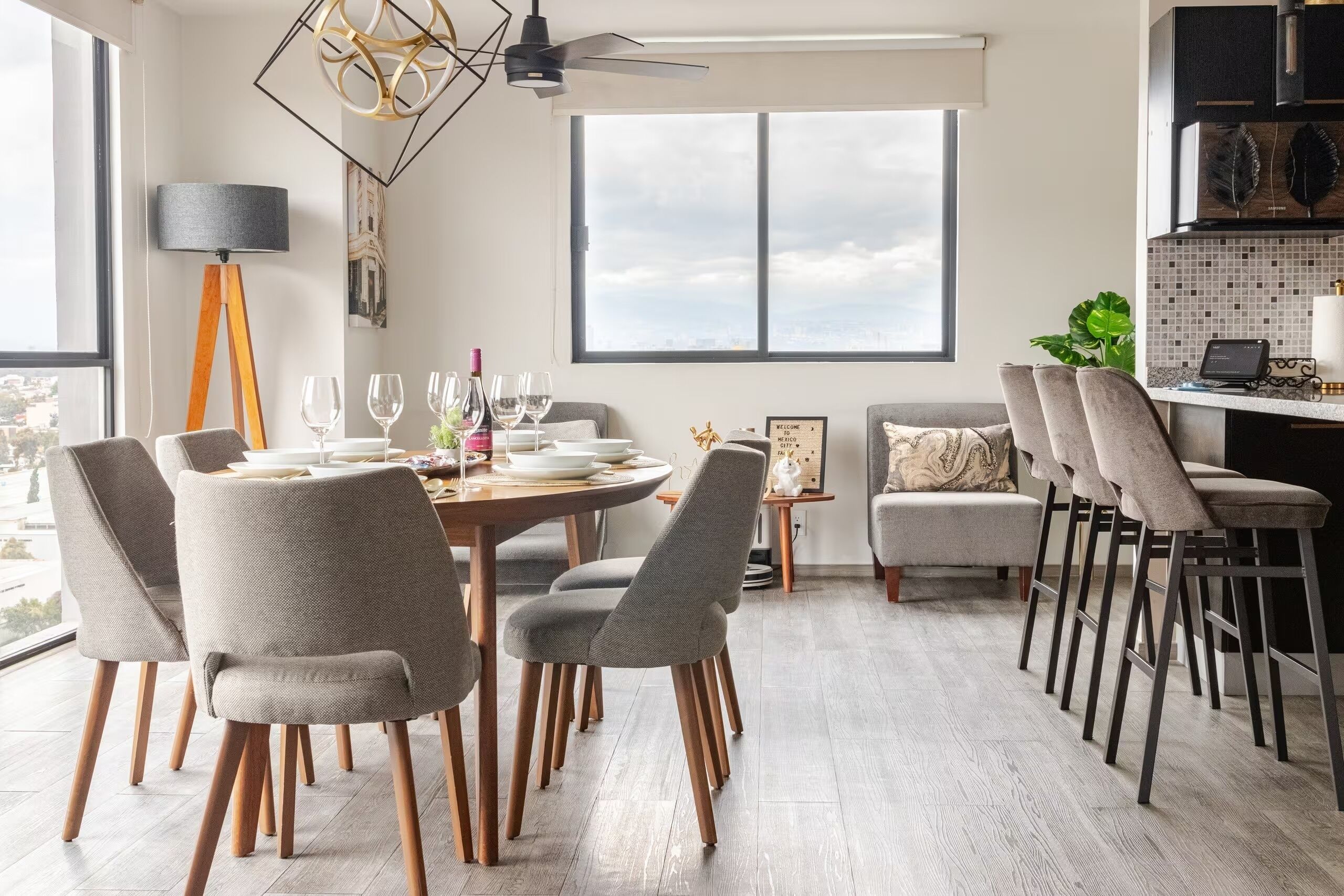 A modern dining area with a round table, multiple chairs, and a view of the city through large windows.