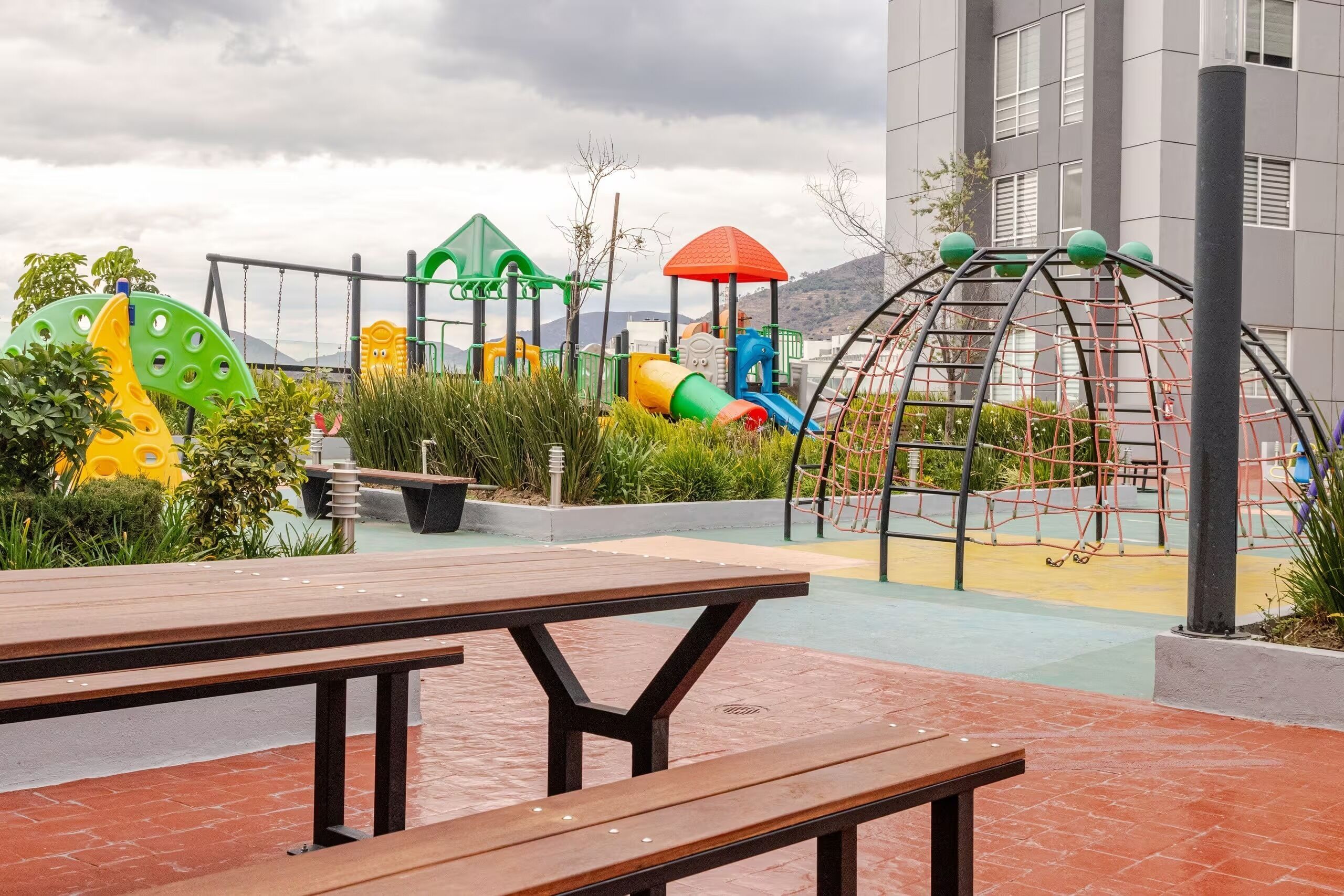 A playground with various play structures, a picnic table, and a building in the background.