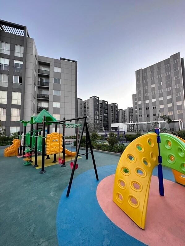 A playground with colorful equipment, surrounded by modern apartment buildings.