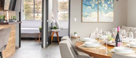 A modern dining area with a wooden table set for a meal, a large abstract painting on the wall, and a view of the outdoors through a glass door.