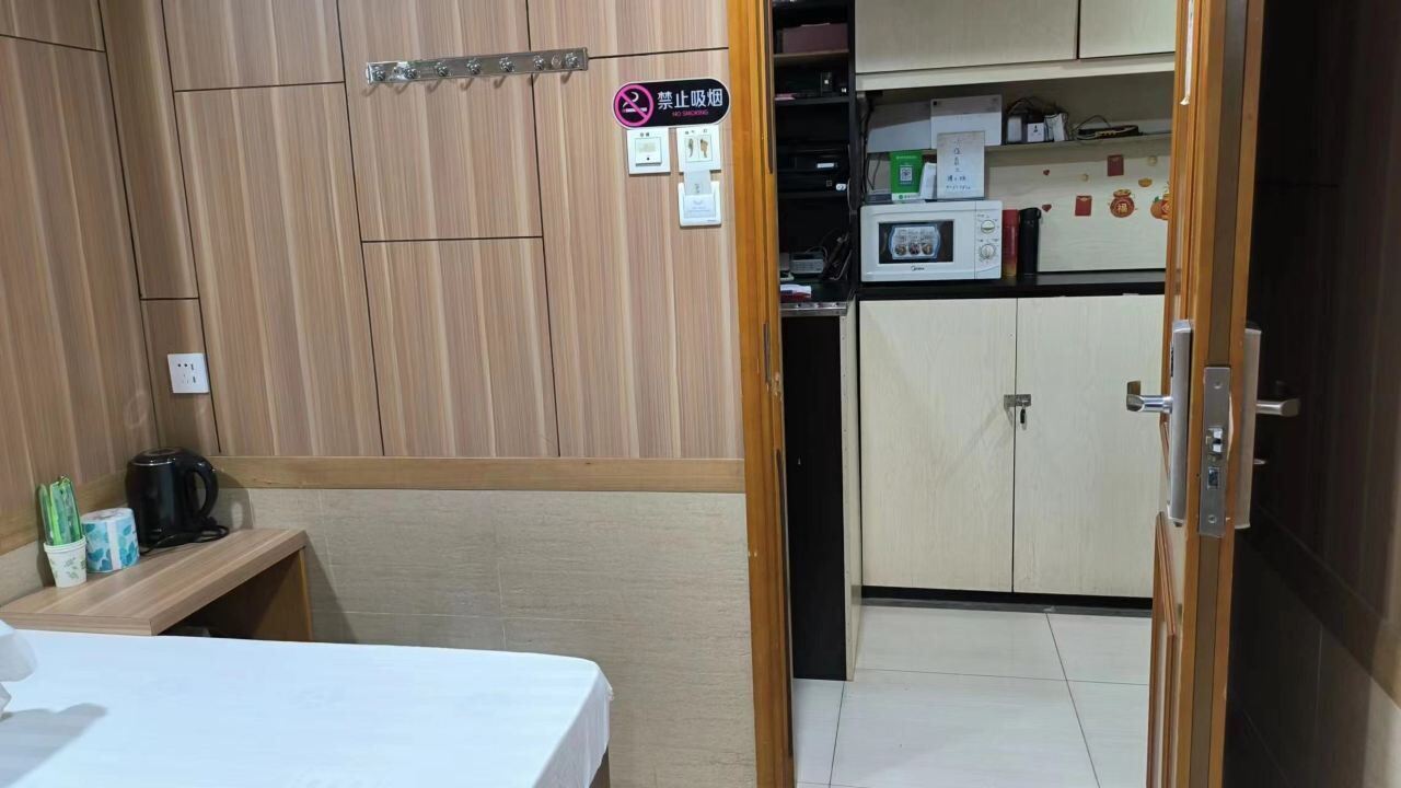 A room with a bed, a desk, a kitchenette with a microwave, and a cabinet.