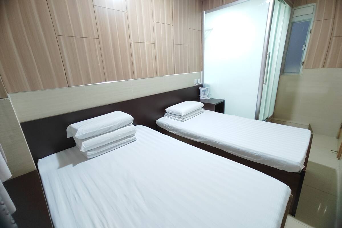 A hotel room with two single beds, a bedside table with a lamp, and a wardrobe.