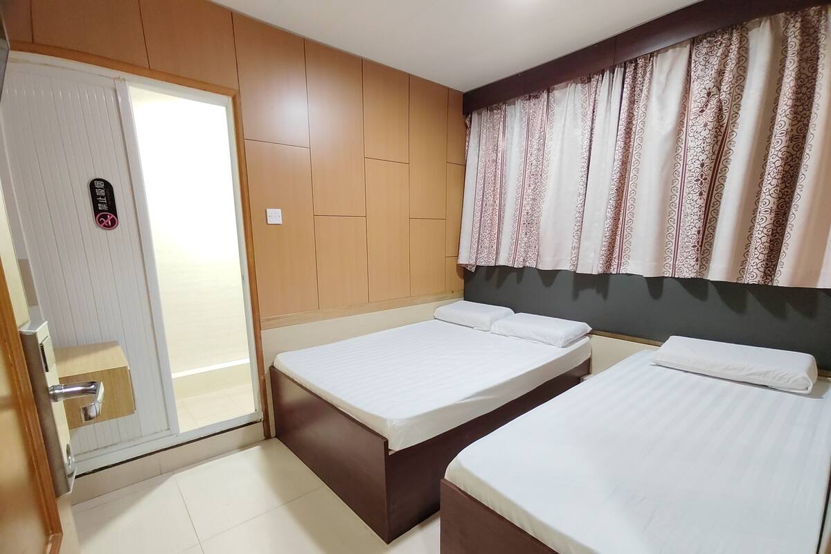 A hotel room with two single beds, a wooden panel wall, a patterned curtain, and a door with a sign.