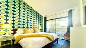 Quarto de hotel com cama, mesa de cabeceira, escrivaninha e vista para o exterior.
