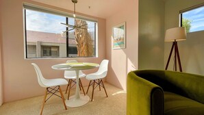 Quarto moderno com uma mesa redonda, cadeiras brancas, uma poltrona verde e um abajur.