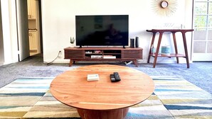 Uma sala de estar com uma grande televisão de tela plana, uma mesa de centro de madeira e um tapete listrado.