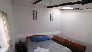A bedroom with a wooden bed, a small bedside table, and a wall-mounted shelf.