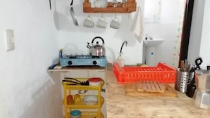 A compact kitchen with a gas stove, kettle, and a yellow rack with dishes.