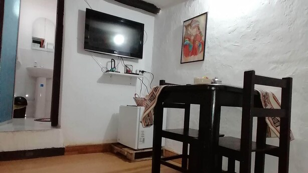 A living room with a wooden floor, a white wall, a flat-screen TV mounted above a white cabinet, and a wooden dining table with chairs.