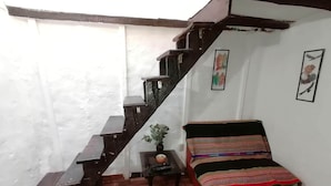 A room with a wooden staircase, a bed with a colorful striped blanket, a small table with a plant, and framed pictures on the wall.