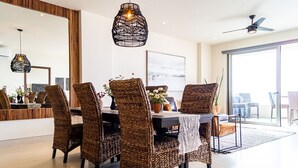 A dining area with wicker chairs, a table with a lace tablecloth, and hanging pendant lights. - Fabulous Cabo condo with amazing view of lands end! (Cabo San Lucas)