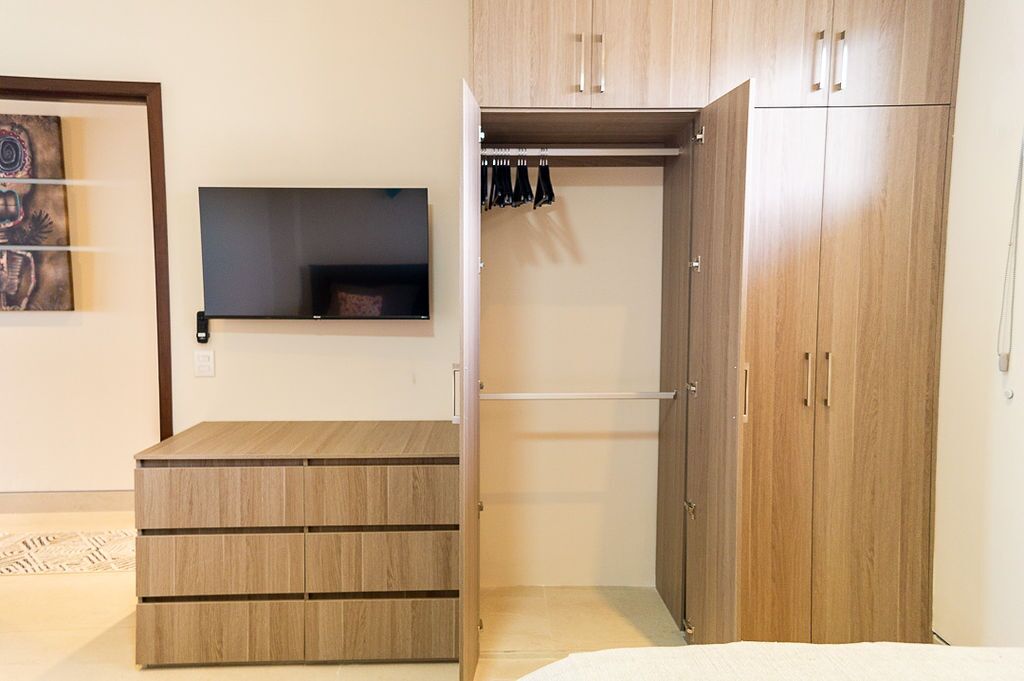 Un dormitorio con un aparador de madera, un armario con espacio para colgar y un estante sobre el aparador.