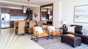 A modern kitchen with dark wood cabinets, a central island, and a dining area with wicker chairs and a coffee table. - Fabulous Cabo condo with amazing view of lands end! (Cabo San Lucas)