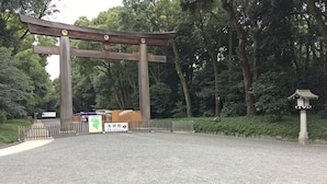 Ein traditionelles japanisches Torii-Tor am Eingang eines Parks, eine Schotterstraße führt hindurch.