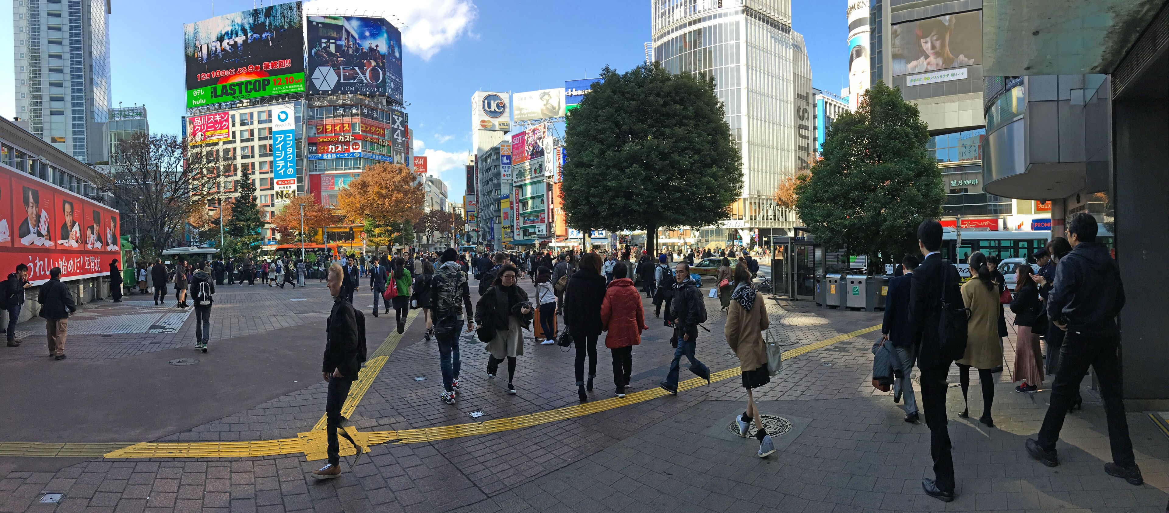 A busy urban square with pedestrians, tall buildings, and various advertisements.