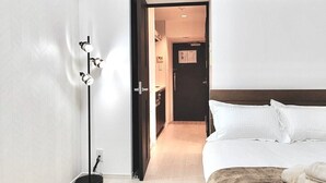 Ein modernes Hotelzimmer mit einem großen Bett, einer stehenden Stehlampe und einer Tür zu einem Flur.