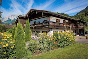 A traditional Alpine-style building with a balcony, surrounded by well-maintained gardens and mountains in the background.