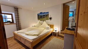 Een slaapkamer met een houten bed, een nachtkastje met een lamp, een hartvormige decoratie en een raam met gordijnen.