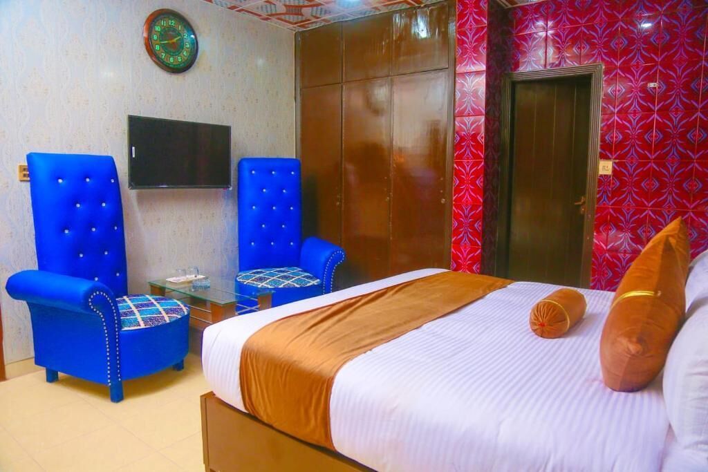 Habitació d'hotel amb un llit, dues butaques blaves, una taula petita, una televisió i un armari.