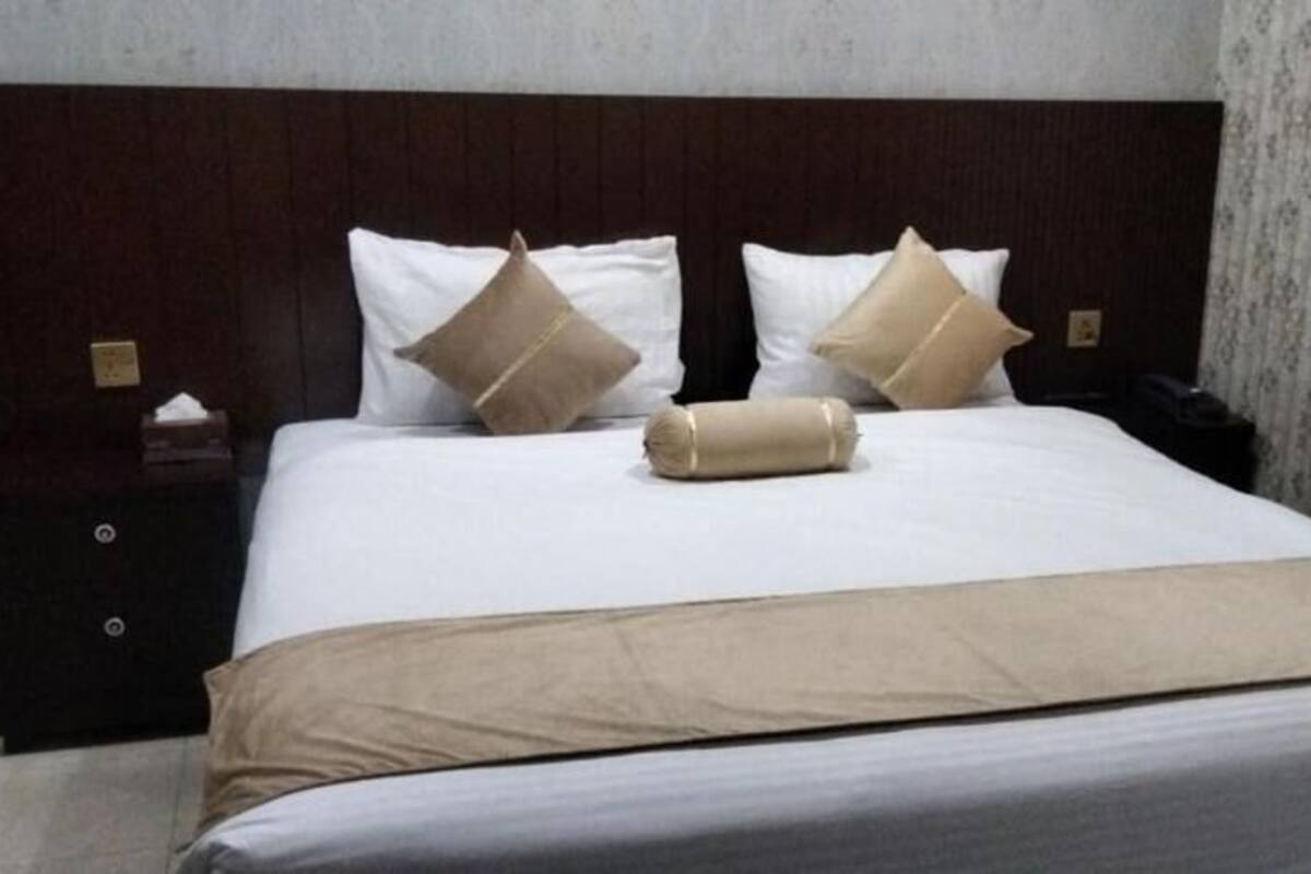 Una cama bien hecha con cabecera de madera, dos mesitas de noche y un papel tapiz con estampado floral.