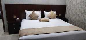 A neatly made bed with a wooden headboard, two bedside tables, and a floral-patterned wall. - Classio Motel (Lahore)