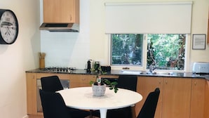 A modern kitchen with a round dining table, black chairs, wooden cabinets, a gas stove, and a window with a view of greenery.