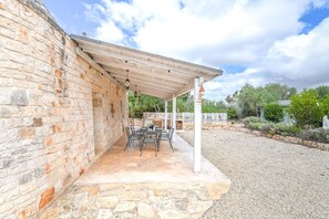 A covered outdoor patio with stone walls, a table with chairs, and a grill area.