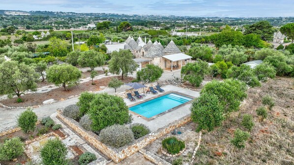 A pool area with lounge chairs, surrounded by stone buildings and trees.