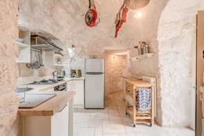 A compact kitchen with a gas stove, a refrigerator, and stone walls.