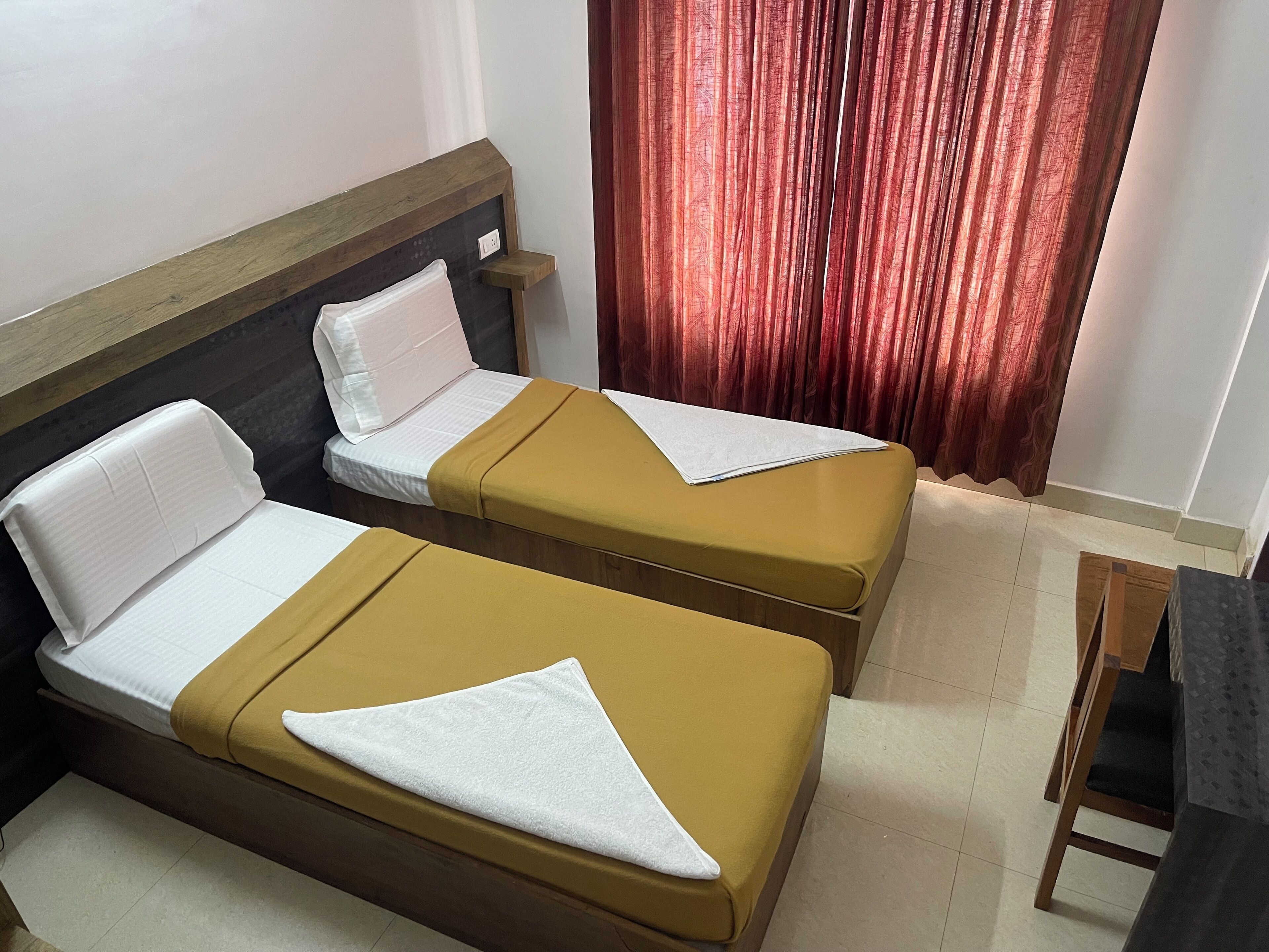Dos camas individuales con cabeceros de madera y almohadas blancas, una mesita de noche de madera y una cortina roja.