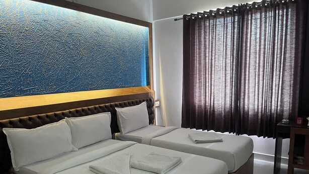 A hotel room with two beds, a large window with curtains, a wooden headboard, and a wall with a textured blue design. - B SIX HOTEL AND LODGE (Bengaluru)