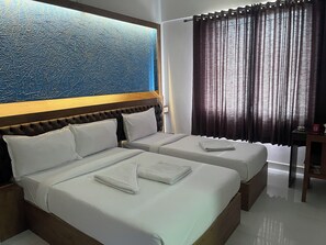 A hotel room with two beds, a large window with curtains, a wooden headboard, and a wall with a textured blue design. - B SIX HOTEL AND LODGE (Bengaluru)