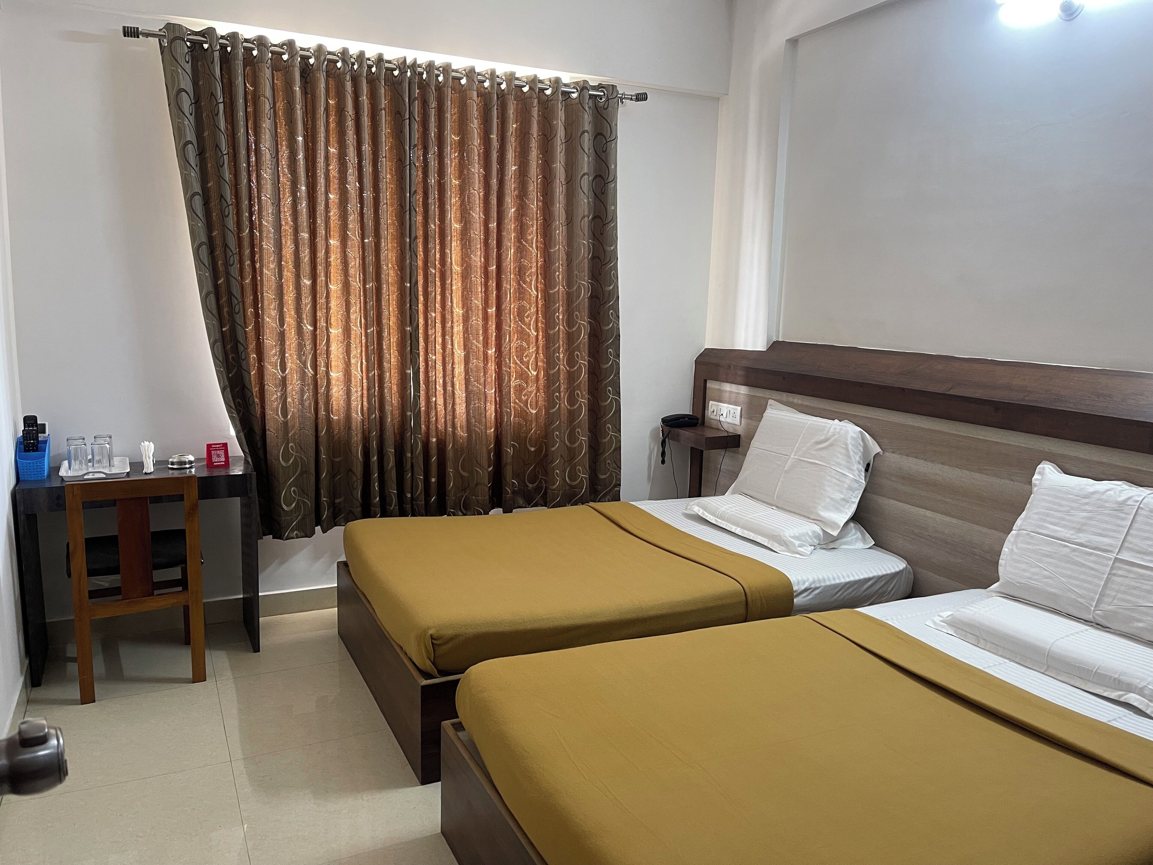 A hotel room with two beds, a desk, a chair, a nightstand, and a curtain.