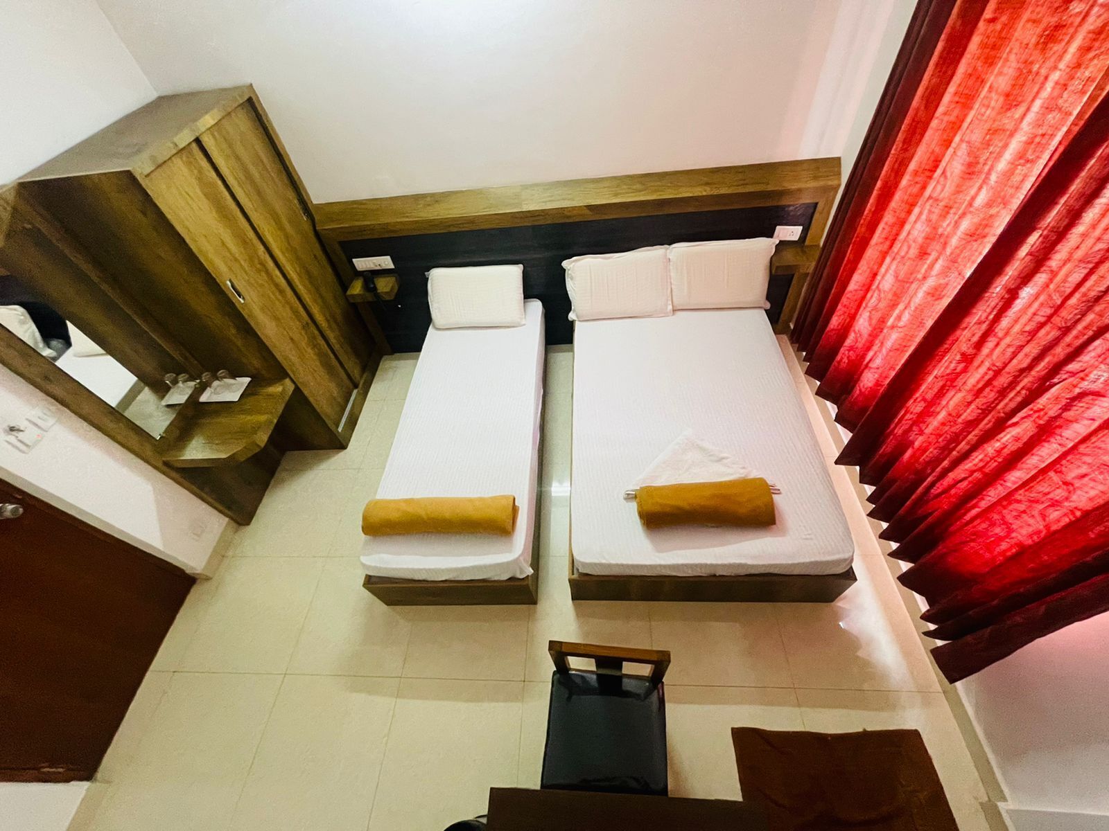 A small, compact room with two single beds, a wooden wardrobe, and a mirror.