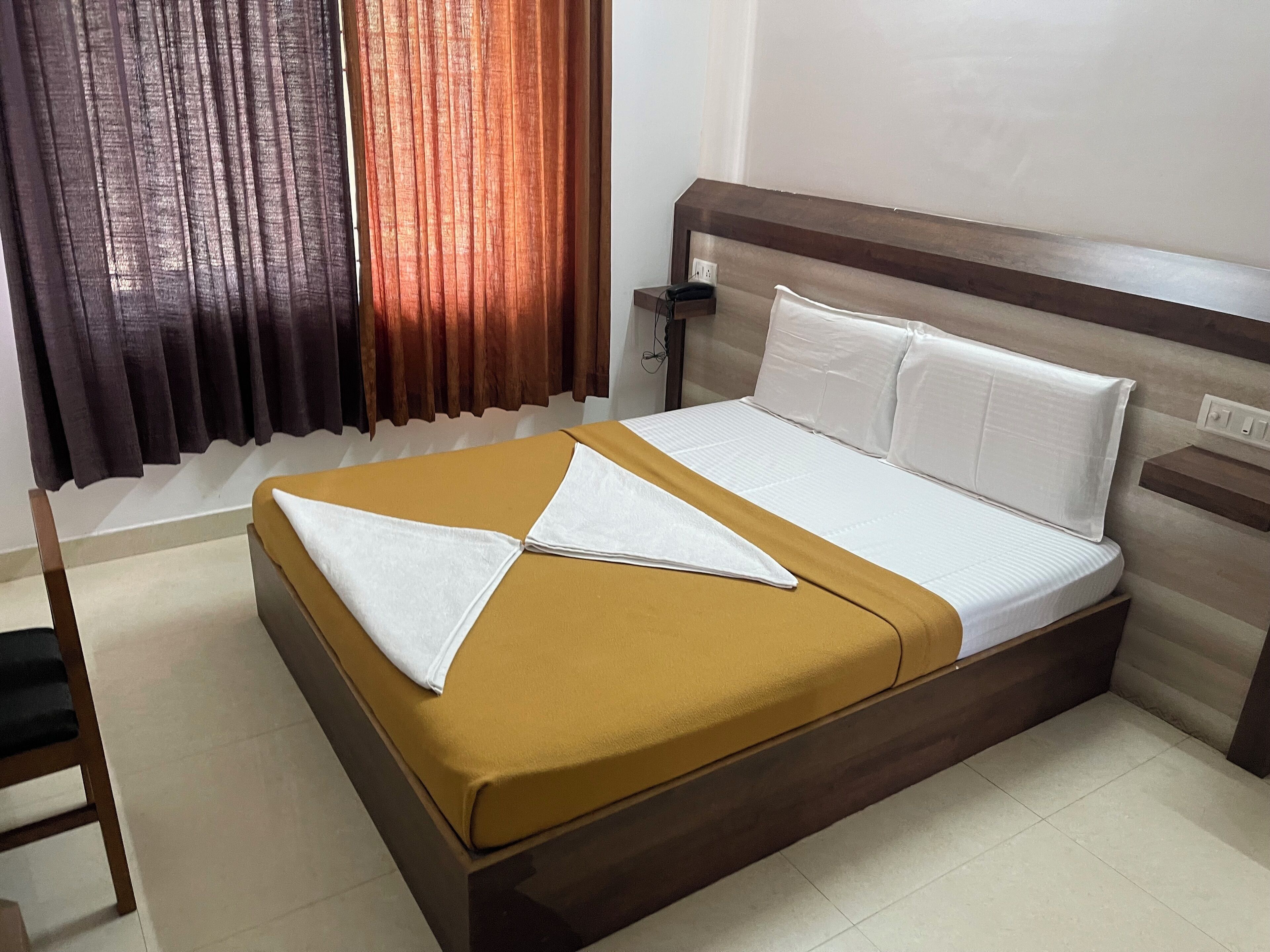 A hotel room with a bed, a nightstand, a chair, and curtains.