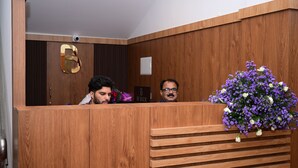 A reception desk with a wooden finish, a number '6' sign, and a floral arrangement. - B SIX HOTEL AND LODGE (Bengaluru)