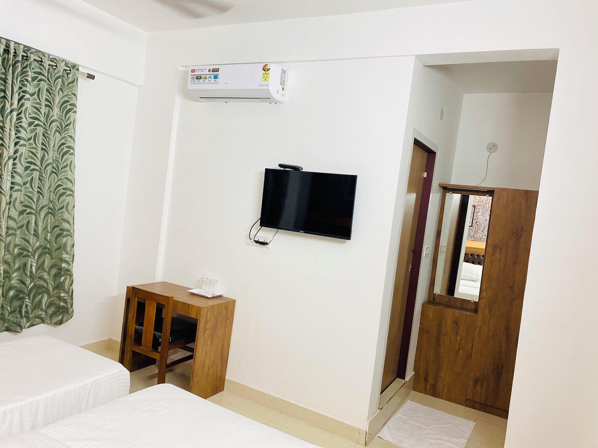 A hotel room with a bed, a desk with a chair, a television mounted on the wall, and an air conditioning unit.